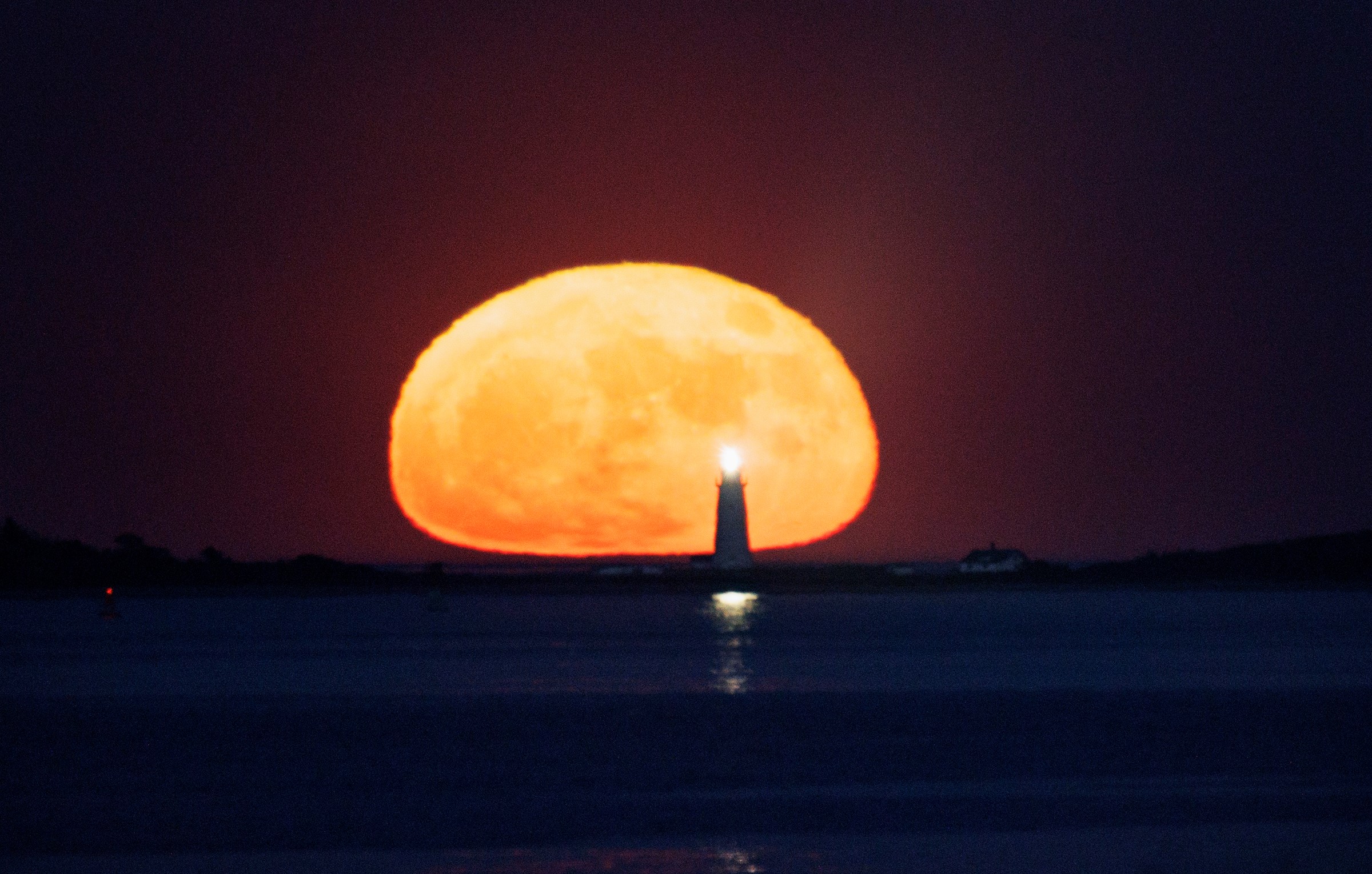 The strawberry supermoon rises over the Boston Light in Boston Harbor on Tuesday, June 14, 2022.