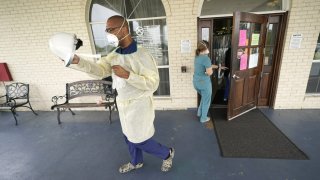 Dr. Robin Armstrong puts on his face shield while demonstrating his full personal protective equipment outside the entrance to The Resort at Texas City nursing home, where he is the medical director, Tuesday, April 7, 2020, in Texas City, Texas.