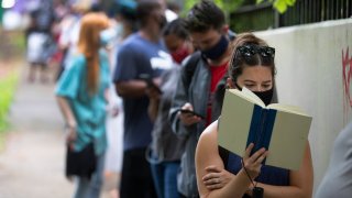 Kelsey Luker reads as she waits in line to vote, Tuesday, June 9, 2020, in Atlanta. Luker said she had been in line for almost two hours.