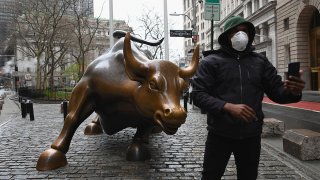 In this March 23, 2020, file photo, a man wearing a face mask takes a selfie at the Charging Bull statue outside the New York Stock Exchange in Manhattan.