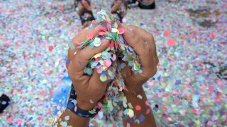A par of hands holds confetti, with more on the ground, during a parade.