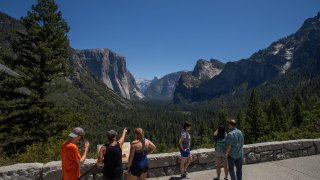 Visitors walk to the Tunnel View lookout in Yosemite Valley at Yosemite National Park, California on July 08, 2020. - After closing for 2½ months because of the coronavirus pandemic, the wildlife is taking over of areas used by the public. The park is open with limited services and facilities to those with day-use reservations, reservations for in-park lodging or camping, and wilderness or Half Dome permits.