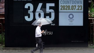 A man wearing a mask against the spread of the new coronavirus walks in front of a countdown calendar showing 356 day to start Tokyo 2020 Olympics Thursday, July 23, 2020, in Tokyo. The postponed Tokyo Olympics have again reached the one-year-to-go mark.