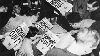 Allied soldiers and others read copies of the Stars and Stripes military newspaper, off the press (belonging to the London Times), that announces Germany's surrender in World War II, London, England, May 7, 1945.
