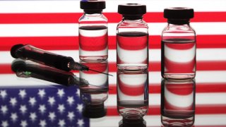 A medical syringe and vials in front of the U.S. flag