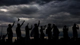 People hold their fists in the air as they shut down I-225 to protest the death of Elijah McClain on July 25, 2020 in Aurora, Colorado. On Friday, prosecutors said Aurora police officers who detained four Black girls by gunpoint after wrongly suspecting they were riding in a stolen car this summer won’t be charged.