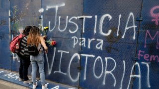 Young women place flowers on the perimeter wall of the Quintana Roo state offices sprayed with graffiti that reads in Spanish "Justice for Victoria," during a protest in Mexico City, Monday, March. 29, 2021. The demonstrators were protesting the police killing in Tulum, Quintana Roo state, of Salvadoran national Victoria Esperanza Salazar when a female police officer knelt on her back to cuff her. Mexican authorities say an autopsy confirmed that police broke her neck.