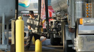 A man moves a fuel hose into position to begin loading gasoline into a tanker truck