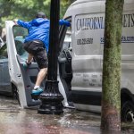A man tries to avoid flood water by hanging onto his car door