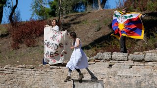 Protesters displaying a Tibetan flag and a banner reading "No genocide games" enter the grounds during the lighting of the Olympic flame at Ancient Olympia site in southwestern Greece