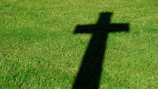 A stark shadow of a Christian cross is projected on a lush green lawn.