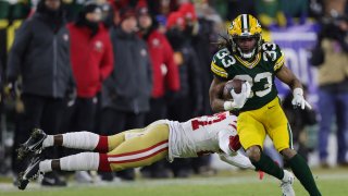 Running back Aaron Jones #33 of the Green Bay Packers carries the ball as he avoids a tackle by defensive back Dontae Johnson #27 of the San Francisco 49ers during the 1st quarter of the NFC Divisional Playoff game at Lambeau Field on January 22, 2022 in Green Bay, Wisconsin.