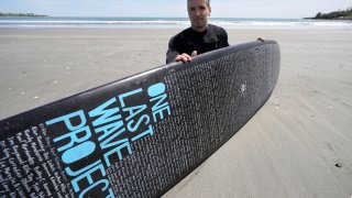 Dan Fischer, of Newport, R.I., sits for a photograph with his surfboard on Easton's Beach, in Newport