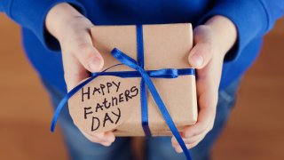 File image of a child's hands holding a gift with kraft paper and tied blue ribbon with a hand-written tag saying "Happy fathers day."