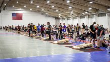 long line of cornhole boards inside a gymnasium, with players lined up throwing bean bags
