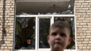 A worker cleans up inside as Tikhon Pavlov, 11, walks past the Kramatorsk College of Technologies and Design