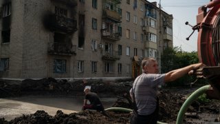 Workers drain water from a crater created by an explosion that damaged a residential building after a Russian attack in Slovyansk, Ukraine
