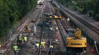Crews work on the tracks at the Wellington T station in Medford, Massachusetts, on Saturday, Aug. 20, 2022, during the first full day of the train line's 30-day shutdown.