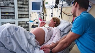 Woman is using laughing gas for laboring in delivery room and holding husband's hand.