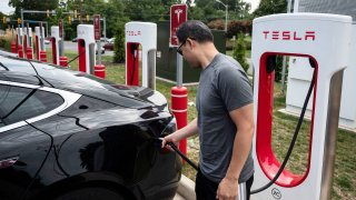 A man charges his car at a Tesla super charging station in Arlington, Virginia on August 13, 2021.