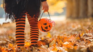 Little girl in witch costume walking outdoors through the fall leaves.