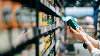 Close up of a woman grocery shopping in supermarket. Holding a tin can and reading the nutrition label at the back