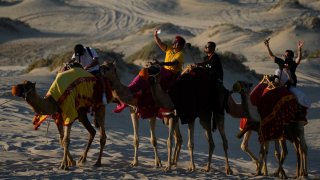 People take selfies while riding camels in Mesaieed, Qatar