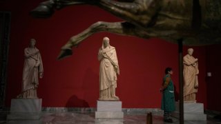 A cleaning woman stands between statues as she watches the presentation event for the planned renovation of the National Archaeological Museum in Athens,
