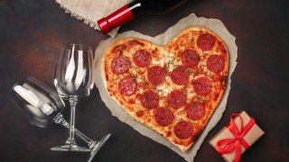 Heart shaped pizza with a bottle of wine, two wineglasses and a gift box.