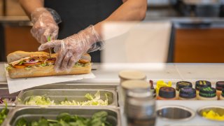 An employee halves a Subway sandwich at a Subway restaurant