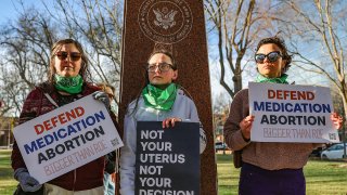 Three members of the Women's March group protest in support of access to abortion medication outside the Federal Courthouse on March 15, 2023, in Amarillo, Texas.