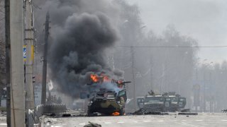 An unidentified soldier’s body lies near a burning Russian Armoured personnel carrier (APC) during fighting with the Ukrainian armed forces in Kharkiv, on February 27, 2022.