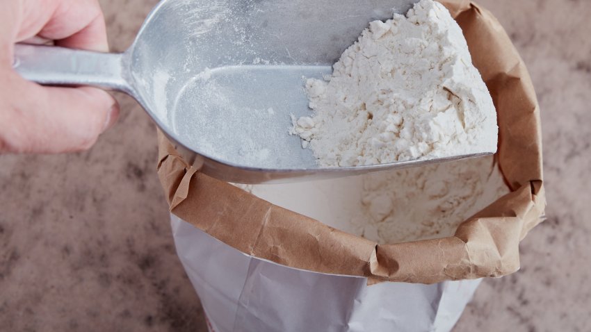 White flour on flour shovel. Opened bag on brownish surface. High point of view.