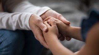 Close up compassionate young foster parent holding hands of little kid girl, giving psychological help, supporting at home. Sincere different generations family sharing secrets or making peace.