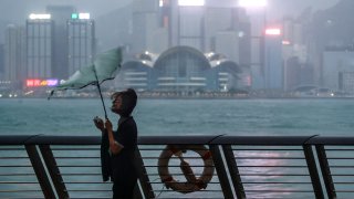 A woman's umbrella is blown at the seaside as typhoon Saola strikes the city with strong winds and rain, in Hong Kong, Friday, Sept. 1, 2023.