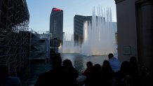 People watch the fountains at the Bellagio hotel-casino behind grandstands installed ahead of the Las Vegas Formula One Grand Prix auto race Friday, Nov. 10, 2023, in Las Vegas. (AP Photo/John Locher)