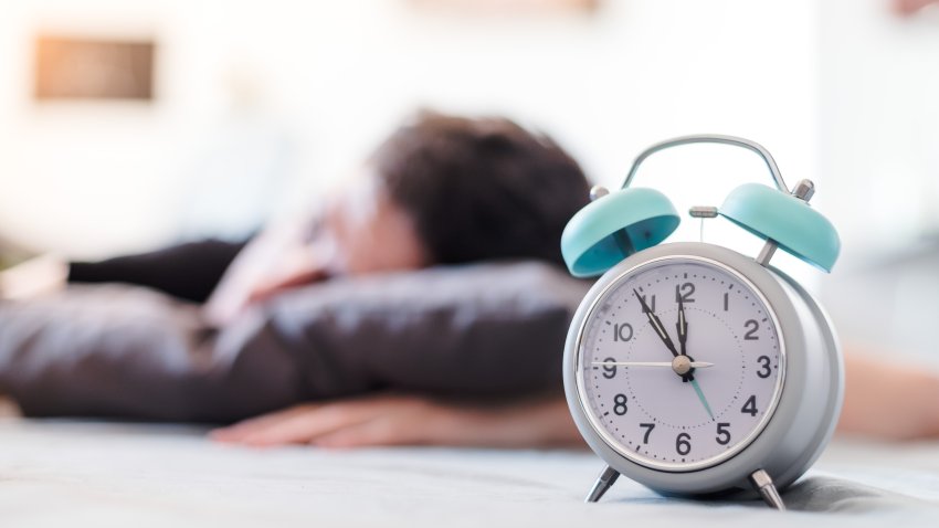 White alarm clock in the morning. Young man sleeps in the background.