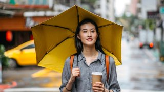 Taiwanese woman walking down the city street with umbrella and coffee on a rainy day