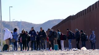 Migrants wait for shuttle buses for transport as they join hundreds of migrants gathering