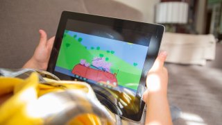 Girl watches “Peppa Pig” on iPad tablet laying in the sofa at home.