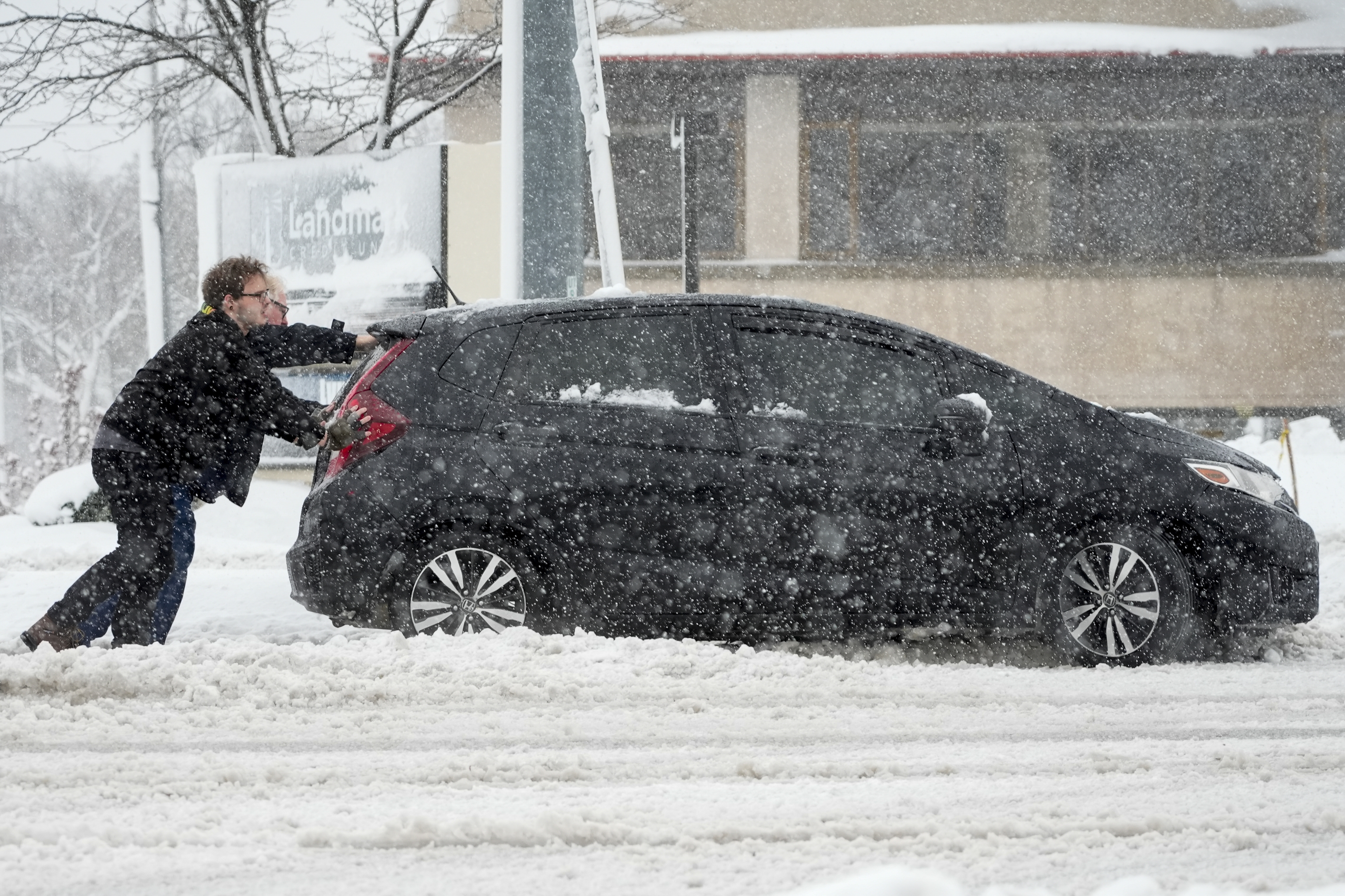 People push a car out of a snowbank as a winter storm arrives Friday, Jan. 12, 2024, in West Allis, Wis.