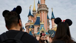 Visitors wearing emblematic Mickey Mouse and Minnie Mouse ears walk in front of the Sleeping Beauty-inspired castle at Disneyland Paris, Oct. 16, 2023.