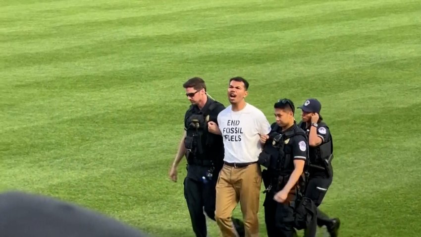 Authorities escort a protestor off the baseball field who wears a shirt reading, "end fossil fuels"