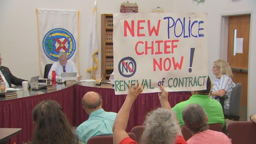 A protester holds up a sign reading "New police chief now!" at the Canton Select Board meeting on Tuesday, June 25, 2024.