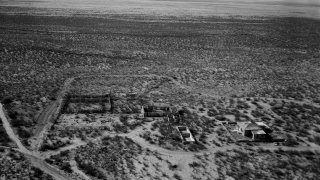 An aerial view (looking south) of the remains of structures, including the McDonald ranch house, at the White Sands Missile Range, New Mexico, 1968. The San Andreas range is visible in the distance. In 1945, the site had been used under the codename Trinity to test the first nuclear detonation.