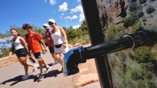 A group of day visitors walk past a closed water bottle tap along the Rim Trail