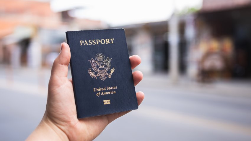 Human hand holding a blue American passport in front of a blurry background