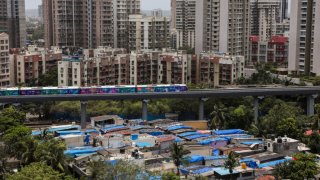 A metro train moves past buildings and slums, in Mumbai, India, 18 June, 2023. 