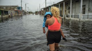 A woman carries a child as she wades through a street flooded in the passing of Hurricane Helene, in Batabano, Mayabeque province, Cuba,