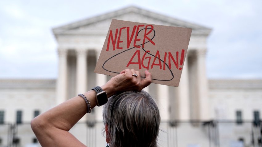 A pro-choice demonstrator holds a sign with a coat hanger, a symbol of the reproductive rights movement, with the words "Never Again" in front of the US Supreme Court